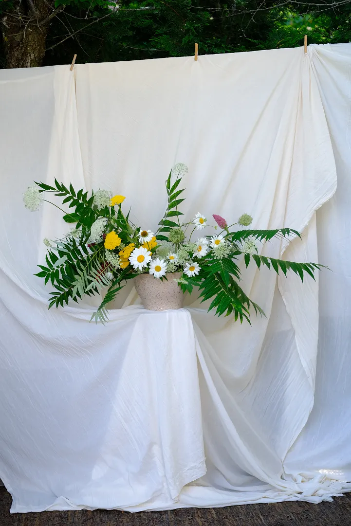se trouvent dans un vase des fleurs blanches et jaunes avec des feuilles vertes sur un fond de nappe