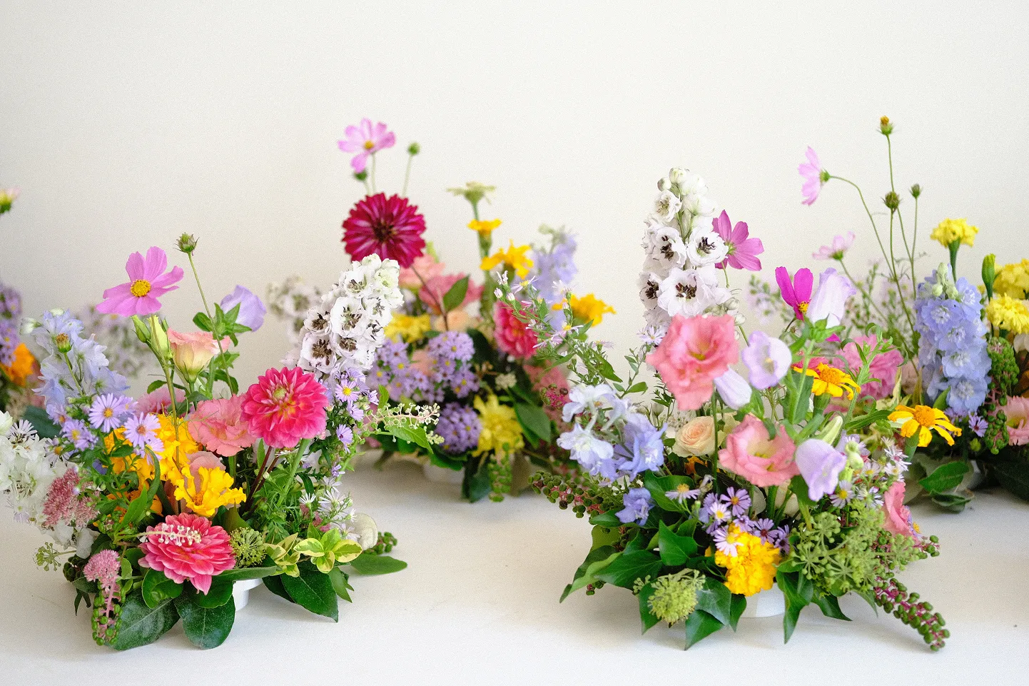 cinq bouquets répartis sur un fond neutre, se composant de multiples fleurs composées des couleurs rose, jaune, rose pâle, violet clair, ainsi que des feuilles vertes