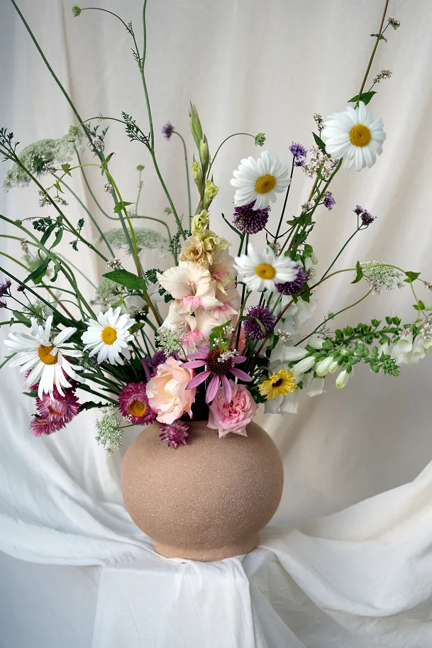 dans un plan rapproché se trouve un vase sur un fond de nappe, comprenant des fleurs de couleur blanche, avec des variations de rose et des tiges et des feuilles vertes