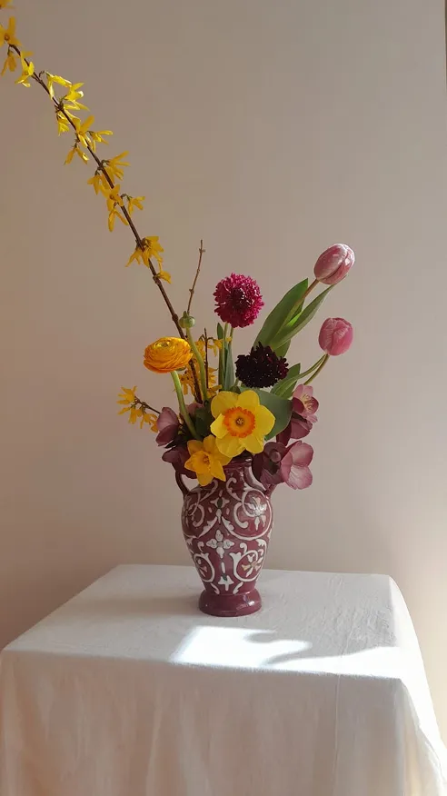 dans un vase de couleur rose avec des détails blancs se trouvent des fleurs composées des couleurs jaune et rose