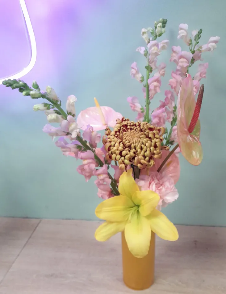un bouquet de fleurs dans un vase jaune éclairé par une lumière, composé des couleurs jaune et rose