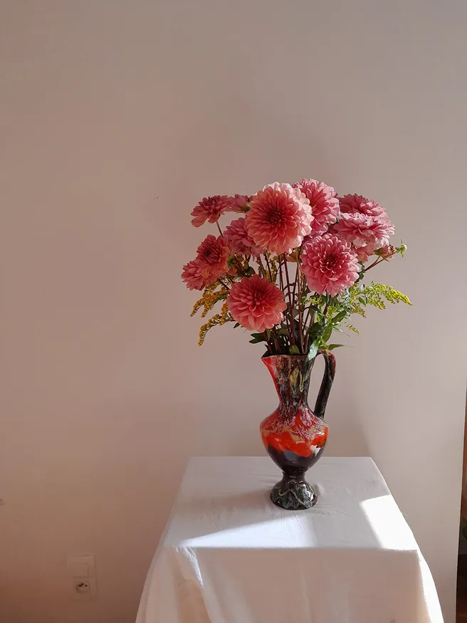 sur une table couverte d’une nappe blanche se trouve un vase rouge avec des fleurs roses