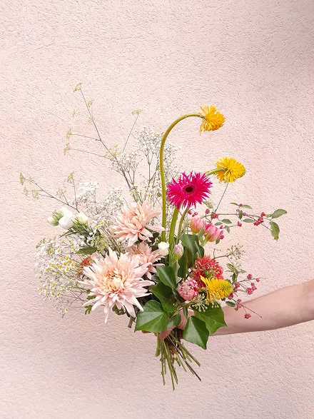 une main tient un bouquet de fleurs composé des couleurs rose et jaune
