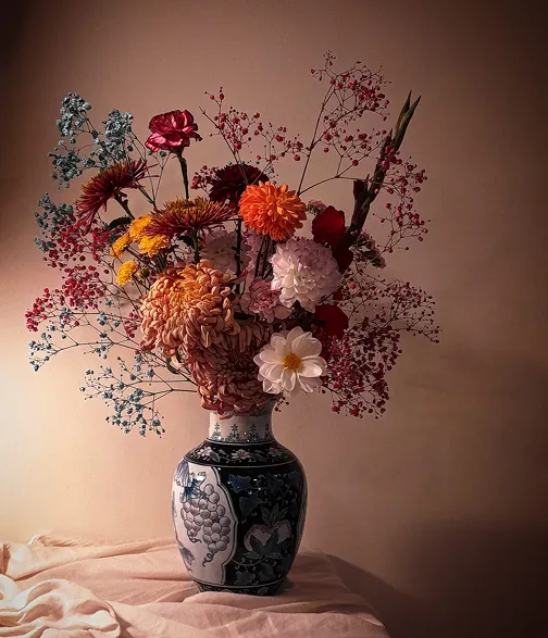 dans un vase bleu et blanc se trouve un bouquet de fleurs composé des couleurs blanc, orange, jaune, rose et myrtille