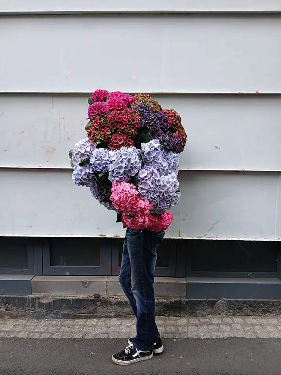 un homme de profil se cache derrière un énorme bouquet comprenant des fleurs roses, violet très clair et violet foncé