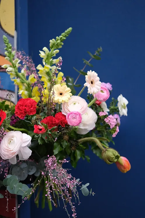 sur fond bleu se trouve un bouquet comprenant des fleurs des couleurs blanc, rouge, jaune et rose