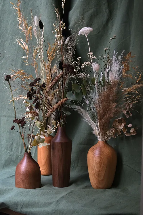 plusieurs vases en bois comportent des fleurs séchées ainsi que des feuilles allant du blanc au marron, en passant par le vert et le jaune