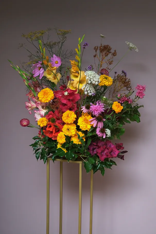 sur un tabouret se trouve un bouquet de fleurs des couleurs jaune, rose, rouge, blanc et marron
