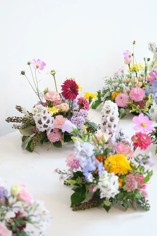 plusieurs petits bouquets sur une table blanche, composés de fleurs blanches, jaunes, roses vives, roses claires et roses pâles avec des feuilles vertes