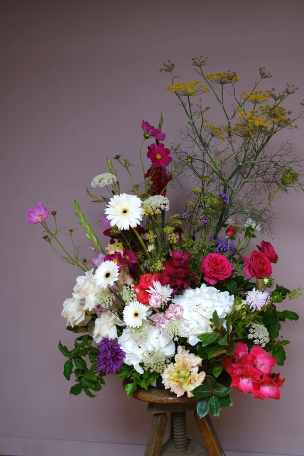 sur un tabouret en bois se trouve un gros bouquet de fleurs, principalement composé de couleurs blanches mais accompagné de fleurs rouges, roses et jaunes