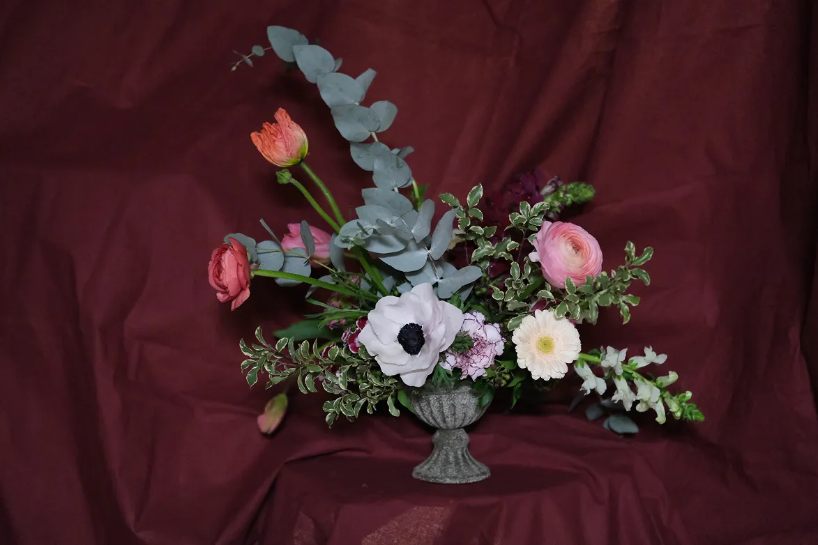 sur un fond rouge se trouve un bouquet de fleurs dans un vase composé des couleurs blanches, rouges et roses avec des feuilles vertes