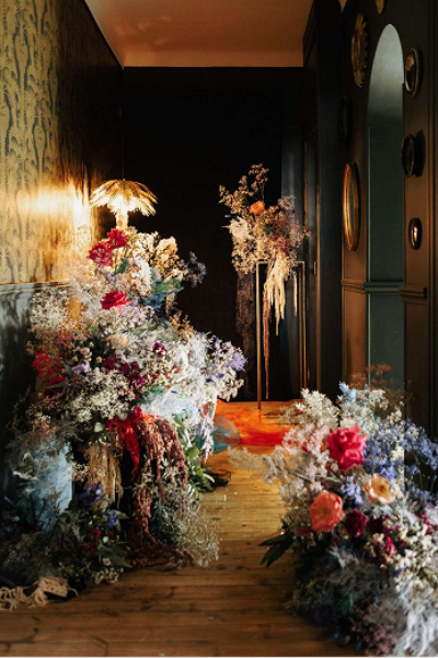 un couloir sombre éclairé par des lumières jaunes et une opulence de fleurs composées des couleurs blanc, rouge, orange, jaune, vert, bleu et violet