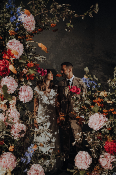 un couple se mariant en arrière-plan avec des fleurs au premier plan, composées des couleurs rose, rouge et bleu