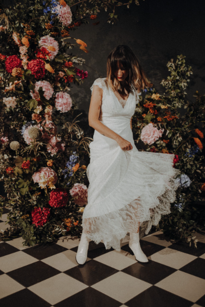 une femme portant une robe de mariée au premier plan, suivie de fleurs composées des couleurs rose, rouge, orange et bleu à l’arrière-plan