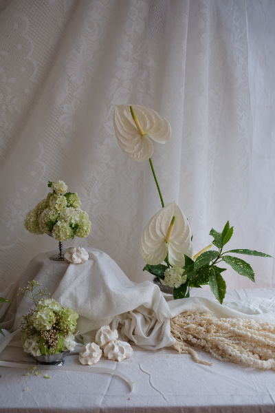 composition florale de fleurs blanches, ainsi que des meringues dans un décor épuré, rempli de nappes et de tissus blancs