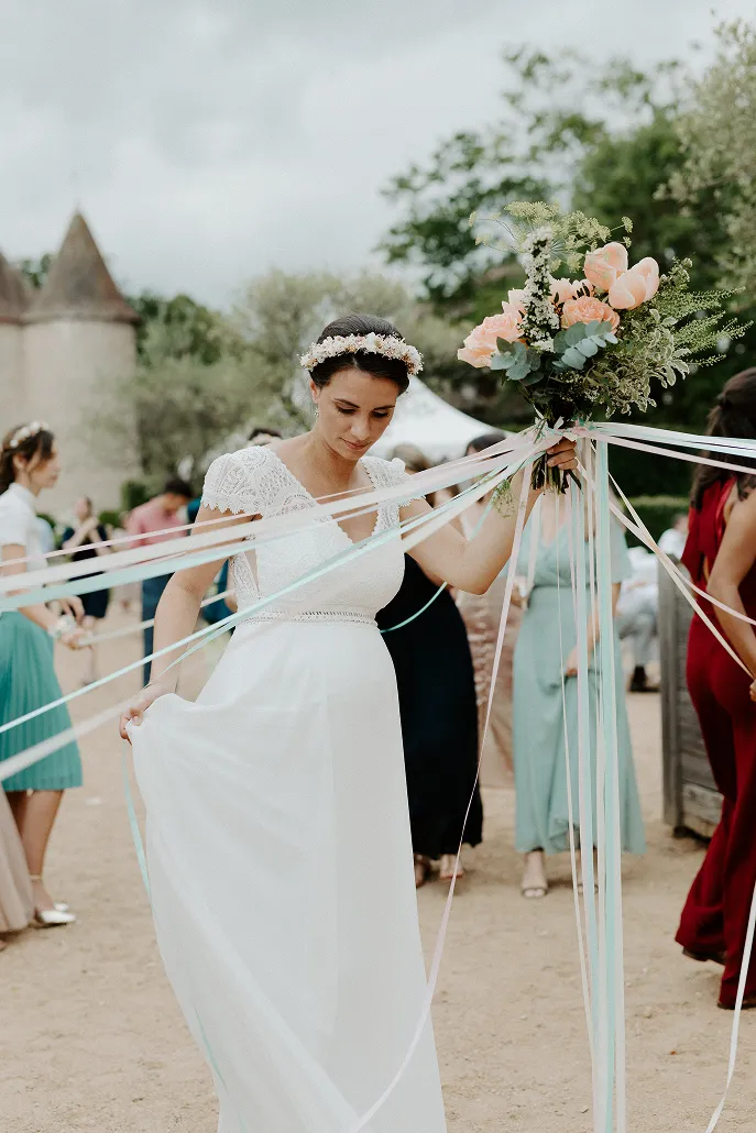 une femme vêtue d’une robe de mariée, tenant un bouquet de fleurs composé des couleurs roses, accompagnées de feuilles vertes, resplendissantes