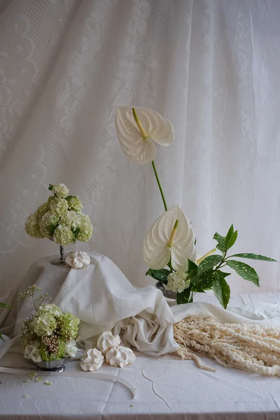 sur un fond blanc, nappé, se trouvent plusieurs fleurs blanches, ainsi que des meringues