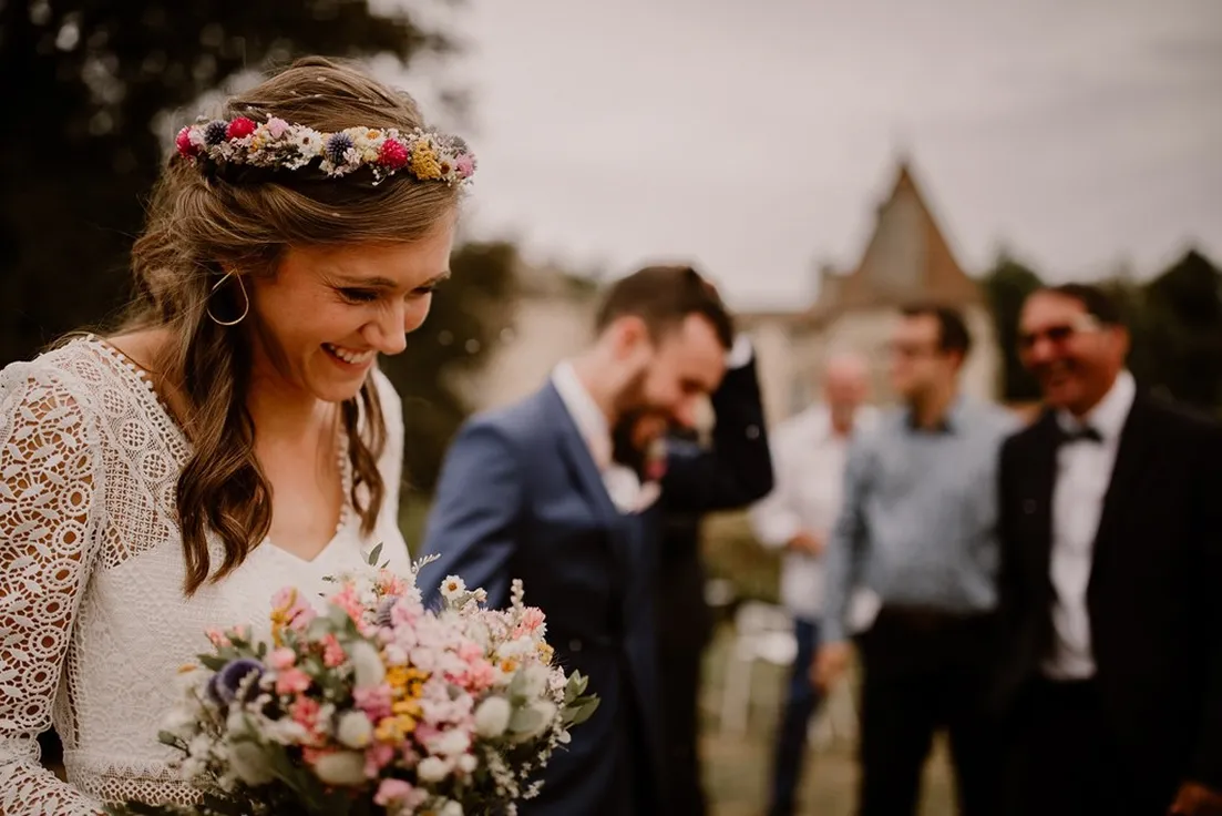 une femme vêtue d’une robe de mariée lors d’un mariage avec un serre-tête en fleurs tient dans ses mains un bouquet de fleurs