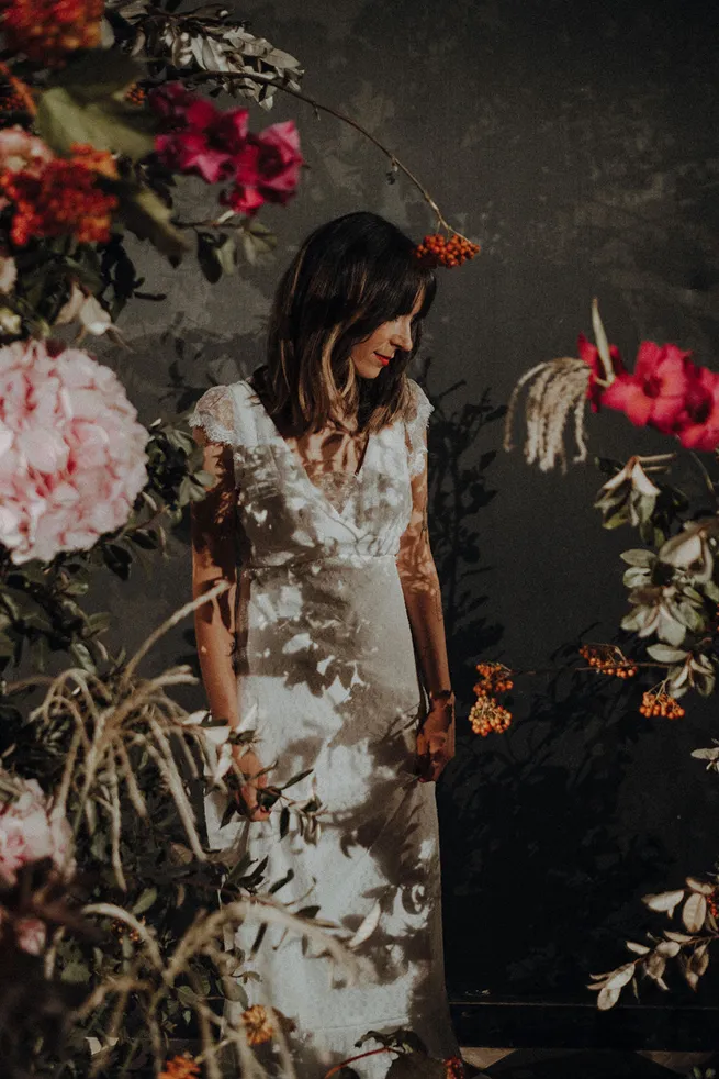 en premier plan, des fleurs de couleur rose et rouge, ainsi que du blanc, et en arrière-plan, une femme lors d’un mariage vêtue d’une robe de mariée, regardant vers le sol