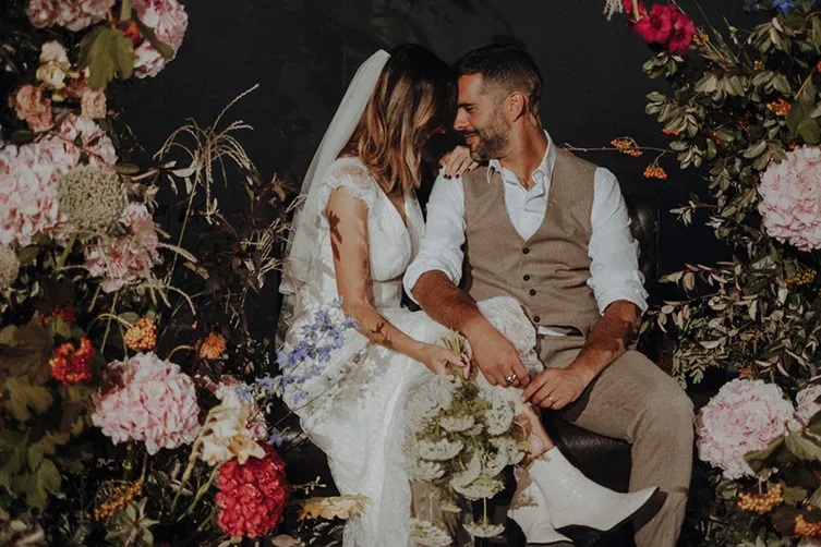 un couple de mariés en arrière-plan, avec au premier plan des fleurs de couleurs rose et rouge dans un décor resplendissant