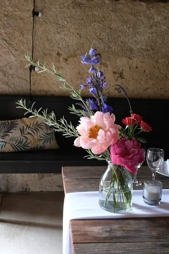 sur une table dressée légèrement, se trouve un vase transparent comprenant quelques fleurs roses, violettes et rouges