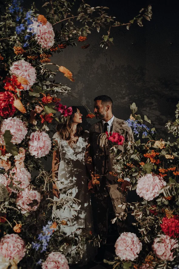 caché par une composition florale, un couple de mariés se regarde tendrement