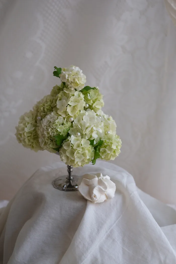 sur un support vêtu d’une nappe blanche se trouvent des fleurs blanches et une meringue