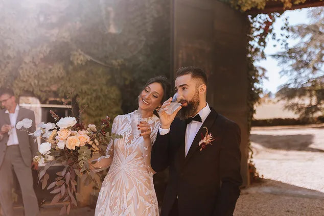 en couple de mariés de face et marchant, la femme tient dans sa main droite un bouquet de fleurs, tandis que l’homme tient dans sa main droite un verre