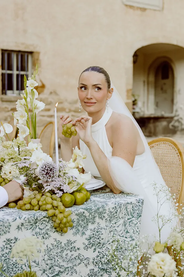 lors d’un mariage, photo de la mariée assise à une table en train de manger du raisin vert